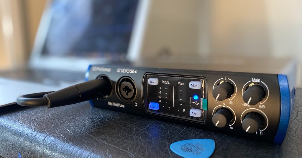 An audio interface with knobs and a cable plugged in, with a laptop behind it.