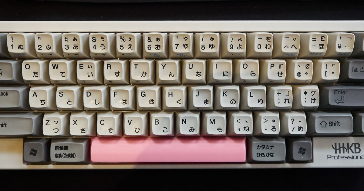 A Happy Hacking Keyboard with gray and white keycaps and a pink spacebar.